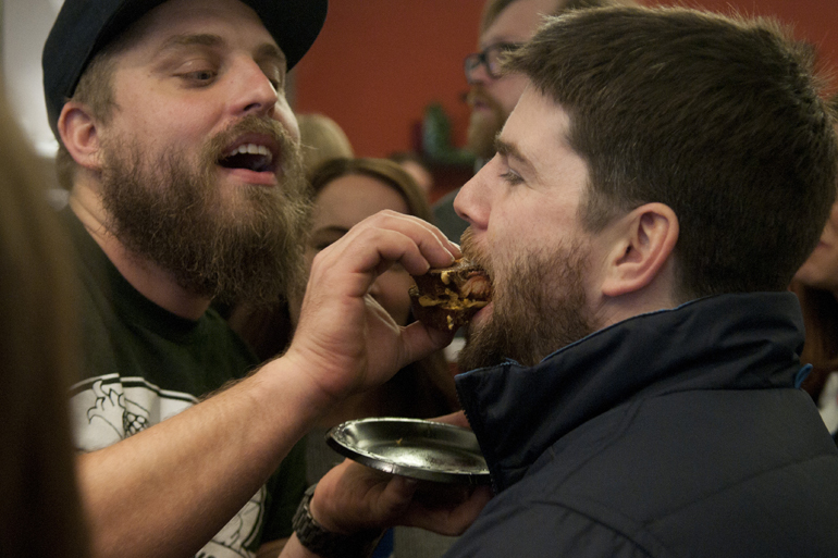 Sun King Brewing employee Biscuit (nickname) feeds a Rueben sandwich to fellow employee Andrew (no last name given) during the Taste of the NFL Sandwich Cook-off at Recess on North College Avenue, Sunday, Jan. 4, 2015.
