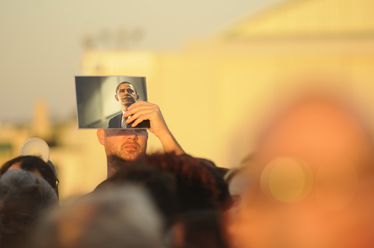 A man shields his face with a picture of President Barack Obama as he waits for Obama to arrive at Burke Lakefront Airport in Cleveland, Ohio.
