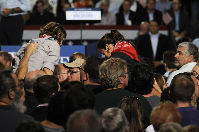 Protesters who were holding up a sign while sitting on shoulders are dragged down as former Mass. Governor Mitt Romney speaks during a presidential campaign stop Sept. 26 in Toledo, Ohio.